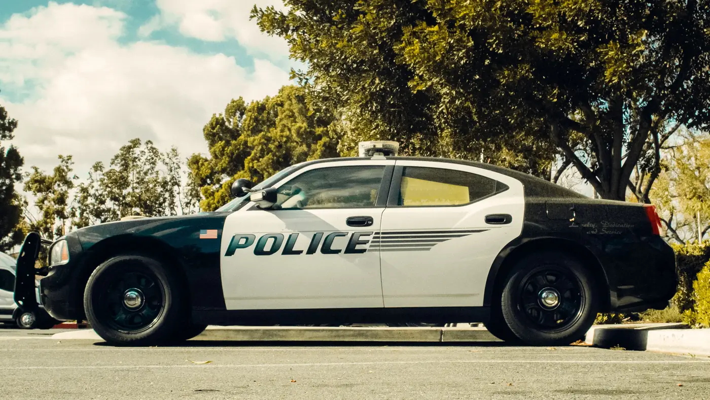 Black and white police car parked in a lot under trees on a sunny day