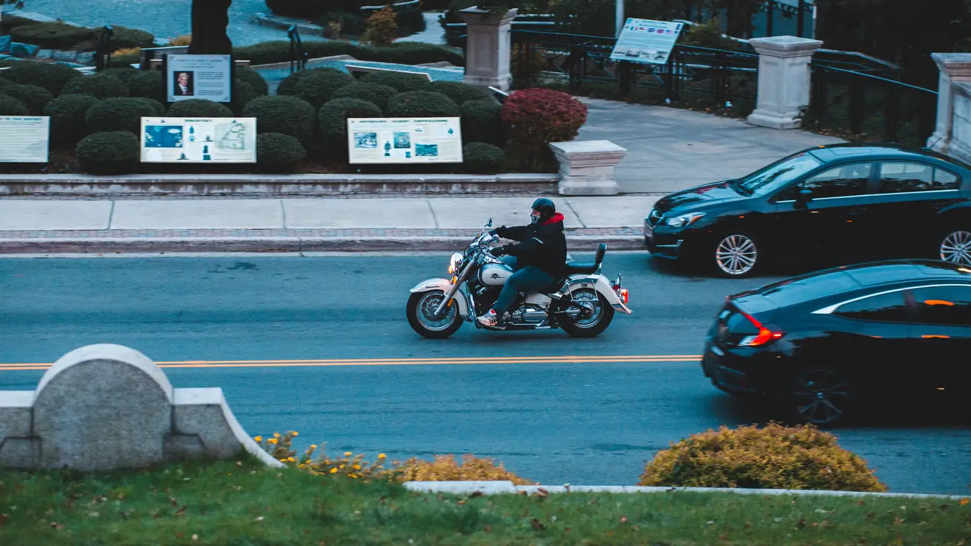 Motorcyclist riding a cruiser on a city street as two cars pass, seen from above