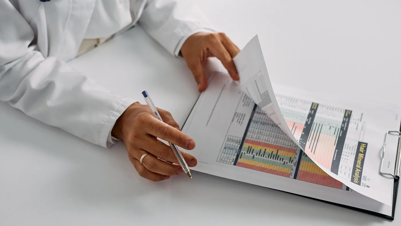 Hands of a doctor in a white coat with a stethoscope reviewing a printed chart with a pen