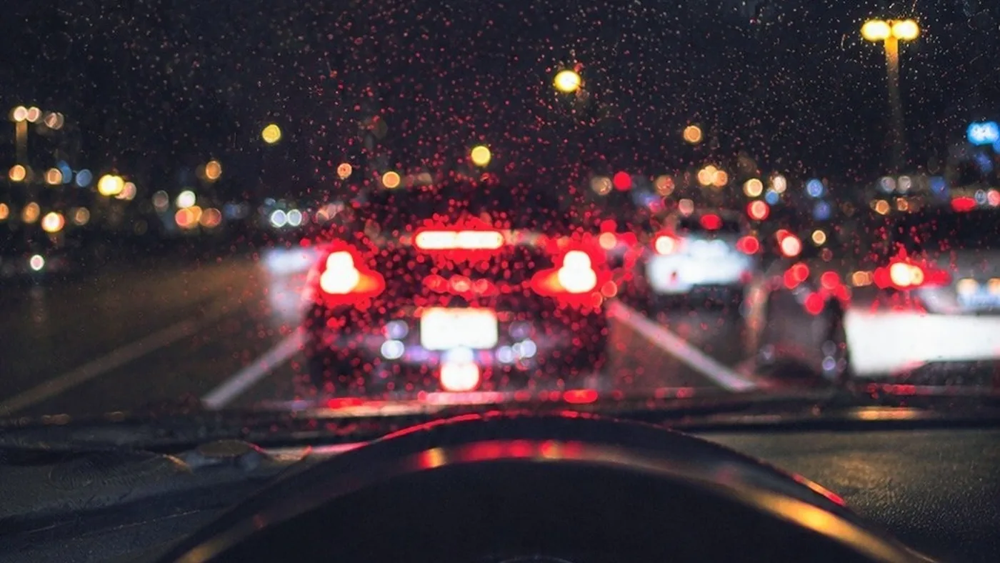 Driver's view through a rainy windshield of brake lights on the car ahead in night traffic