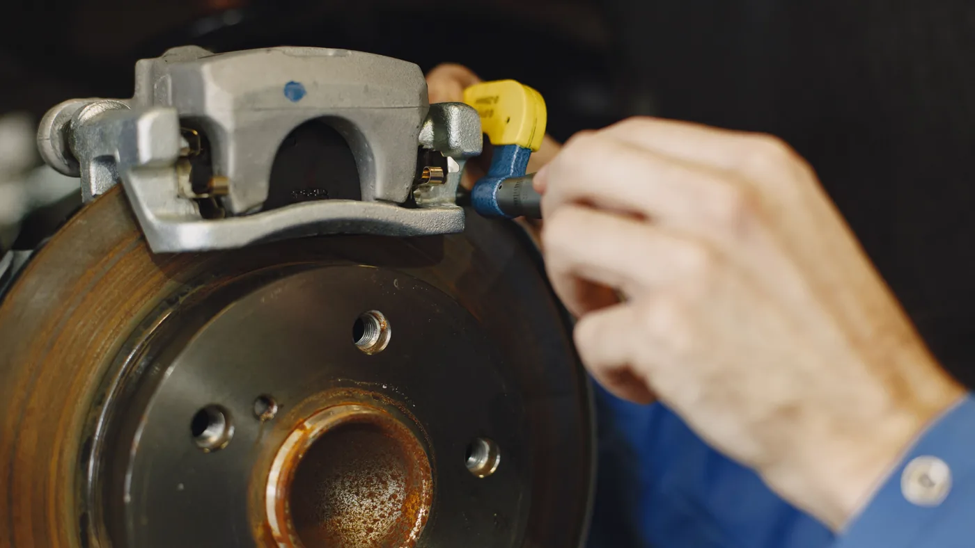 Mechanic's hands inspecting a disc brake caliper and rotor on a car