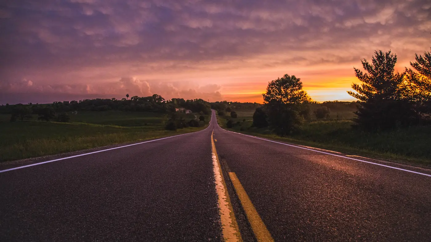 Empty two-lane rural road through green fields at sunset